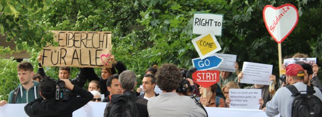 "Bleiberecht für alle" und "for the right to come go stay" steht auf den Schildern der AktivistInnen