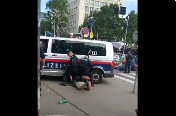 Zwei Beamte drücken einen Aktivisten unter ein Polizeiauto.