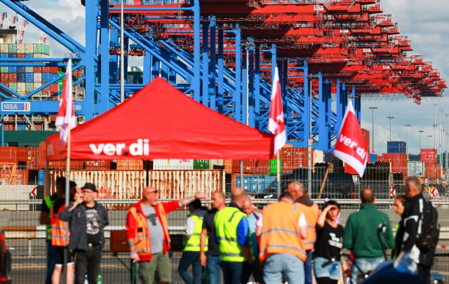 Hamburg: Beschäftigte mit Verdi-Flaggen protestieren bei einem Warnstreik vor einem Container der HHLA (Hamburger Hafen und Logistik AG). Foto: dpa/Christian Charisius