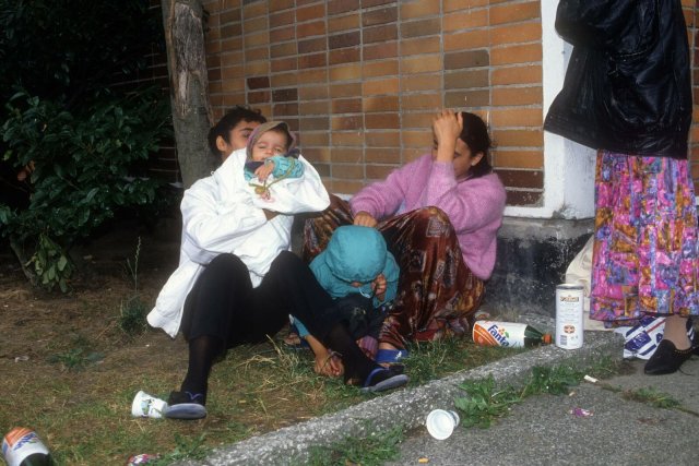 Eine junge Geflüchtetenfamilie vor einem Haus am Boden in Rostock-Lichtenhagen 1992.