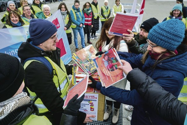 Demonstrierende Erzieher*innen sammeln Druckexemplare des Bildungsprogramms und geben sie an die Landespolitiker*innen zurück.