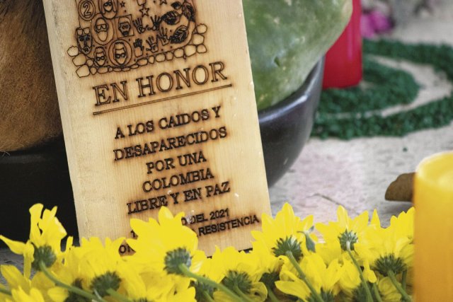»Zu Ehren der Getöteten und Verschwundenen, für ein freies und friedliches Kolumbien« steht auf dem Schild, das bei dem Tribunal von Blumen und Kerzen umrahmt war.