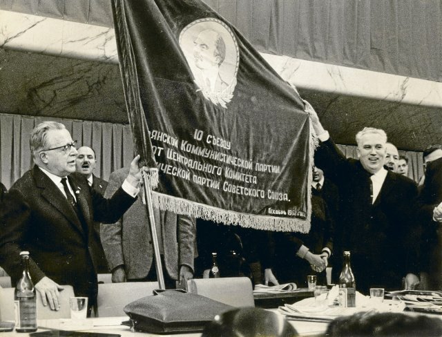Wer wird denn da am Schlaf der Welt rühren? Der Abgesandte der postleninistischen Sowjetunion Frol Kozlow übergibt an den PCI-Politiker Palmiro Togliatti eine Flagge mit dem Konterfei des russischen Revolutionärs.