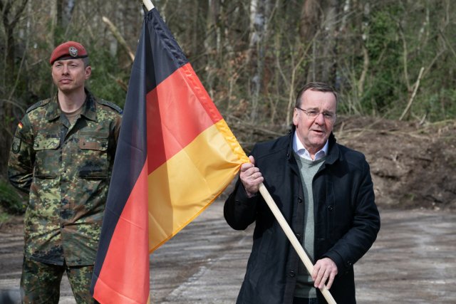 Boris Pistorius (SPD, r), Bundesverteidigungsminister, hält auf dem Gelände eines geplanten Bundeswehrstandorts eine Deutschlandfahne.