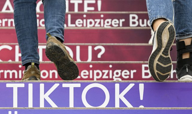 Besucher gehen auf der Leipziger Buchmesse eine Treppe hinauf, die mit Werbung der Video-Plattform TikTok gestaltet ist.
