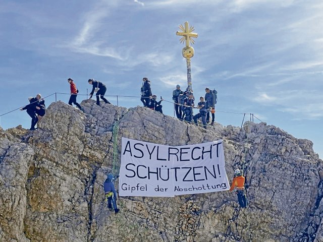 Aktive des Bayerischen Flüchtlingsrats und der Initiative Leave No One Behind entrollten am Freitagmorgen bei einer Kletteraktion auf der Zugspitze in Sichtweite des Ministertreffens ein Protestplakat gegen menschenrechtswidrige Politik.