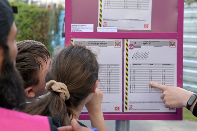 Fahrgäste schauern an einem Bahnhof an einer Haltestelle für Ersatzverkehr auf einen Fahrplan für Ersatzbusse.