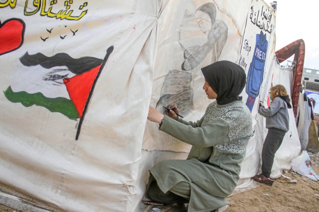 Ein Mädchen malt auf eine Plane. Vertriebene Palästinenser, darunter auch Kinder, die im Yarmouk-Stadion Zuflucht gefunden haben, versuchen, ihr tägliches Leben unter den schwierigen Bedingungen in Gaza-Stadt fortzusetzen.