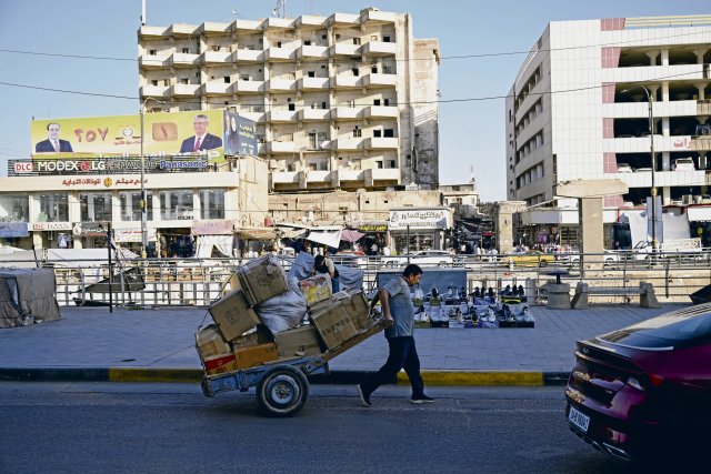 Ein Mann zieht einen mit Kisten beladenen Karren an Wahlplakaten...